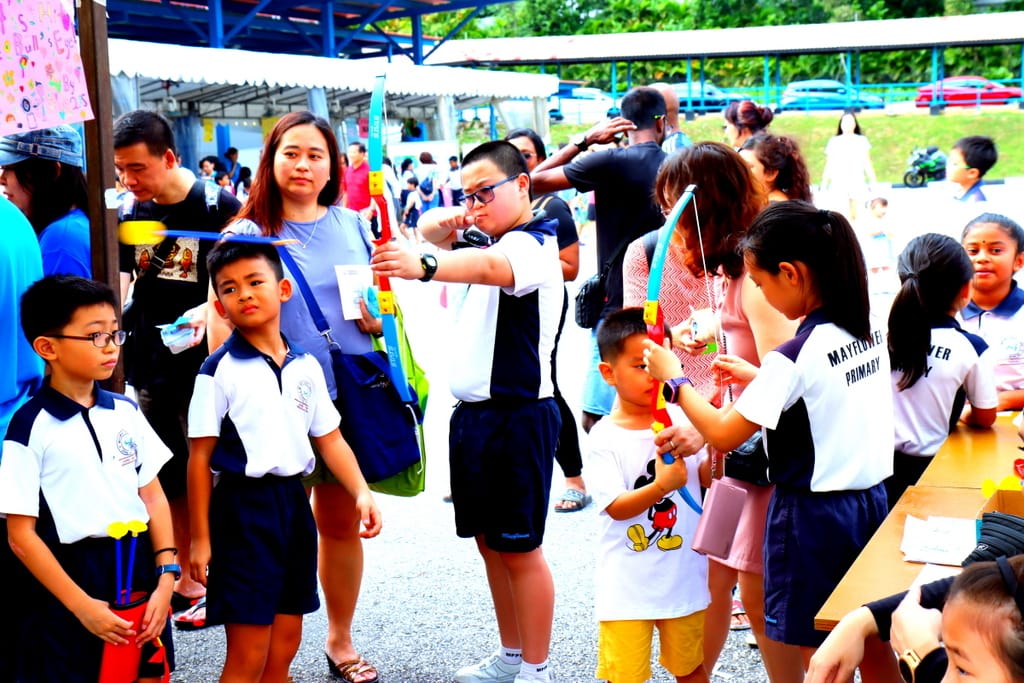Children in Mayflower Primary school uniforms play with toy bows and arrows at an outdoor school event.